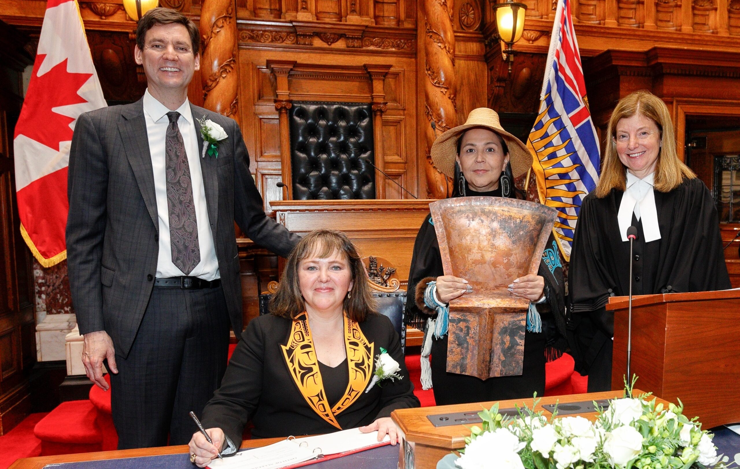 MLA Laanas Tamara Davidson seated in front of Premier David Eby, Legislative Assembly Kate Ryan-Lloyd (far right) and Lucy Bell, who is holding the copper shield created by Haida artist Wiigaanad (Sid Crosby). Photo: Kevin Light.